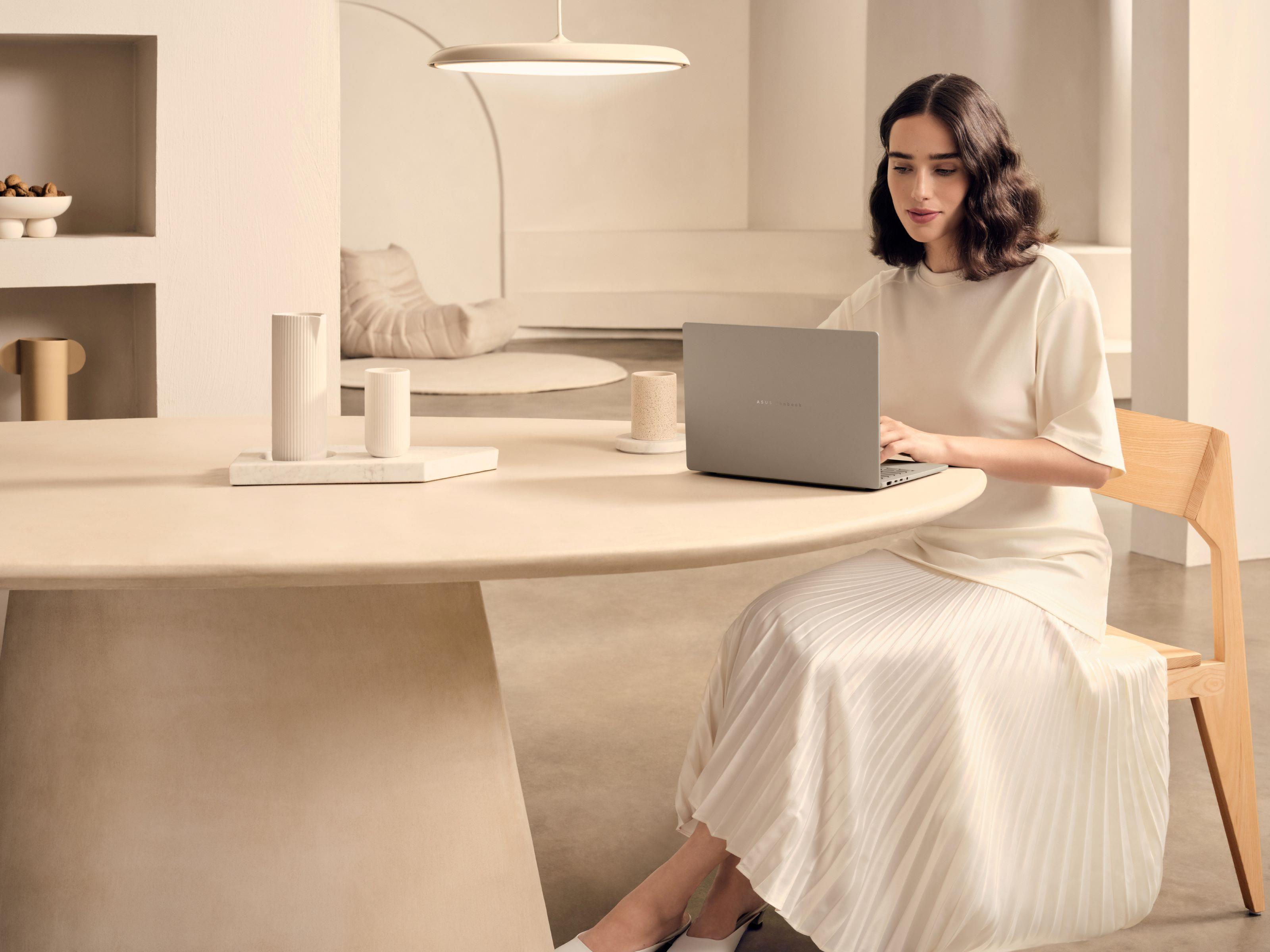 A woman sitting at a table with an ASUS Zenbook A14 in a beige setting